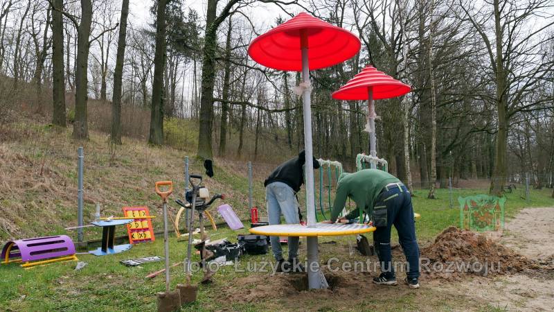dwóch mężczyzn montuje nowe urządzenie na placu zabaw